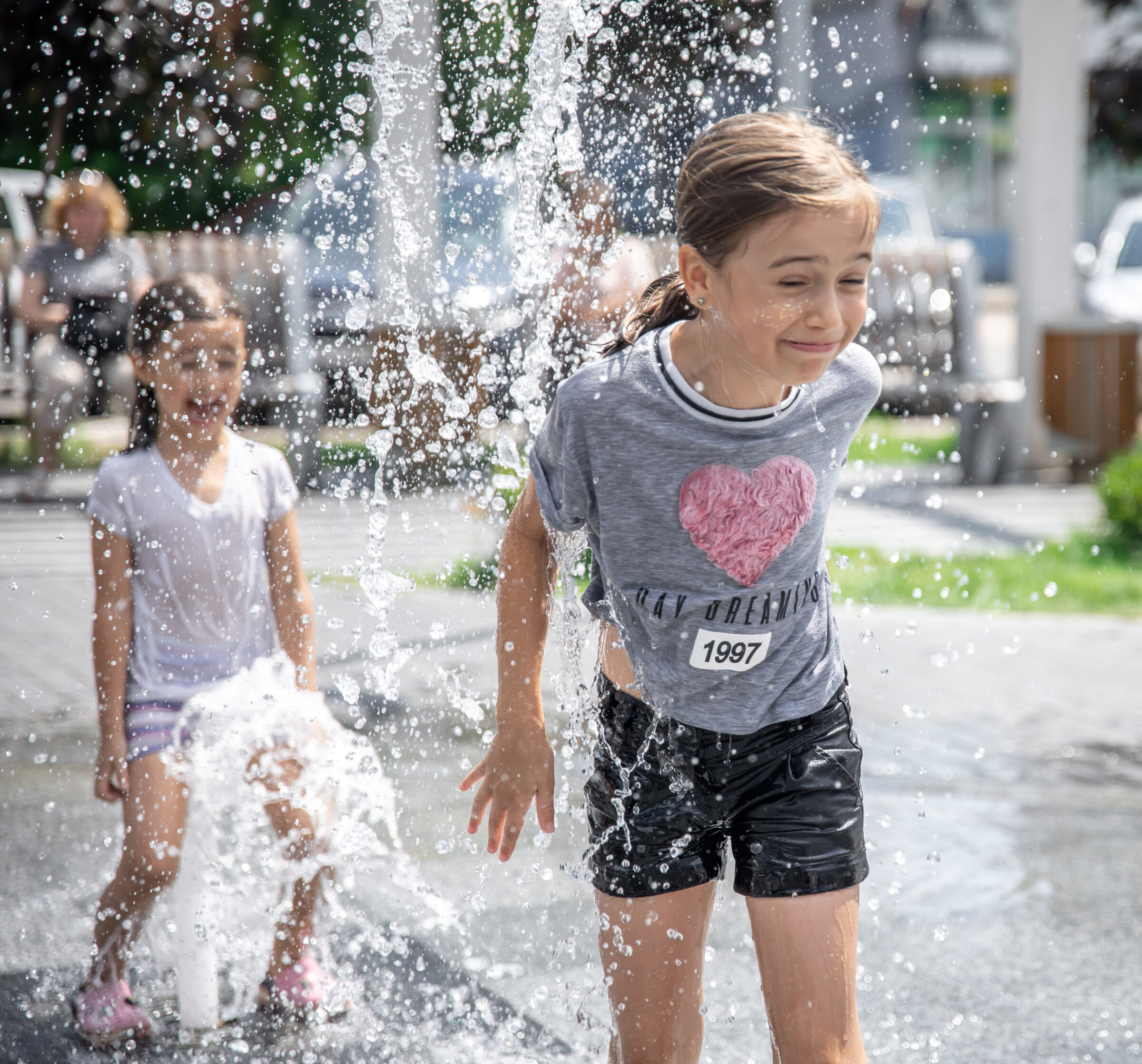 Little girls cool off in a fountain on a hot summer day.